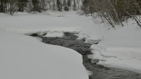 Narrow water stream flows between clumps of white snow Stock Footage 109742376