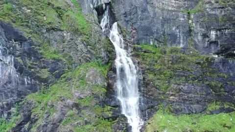A narrow waterfall cascades down a moss-covered rocky cliff face Stock Footage 322954459