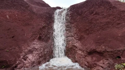 Narrow waterfall falling over red volcanic rock in Kauai Hawaii 動画素材 347826222