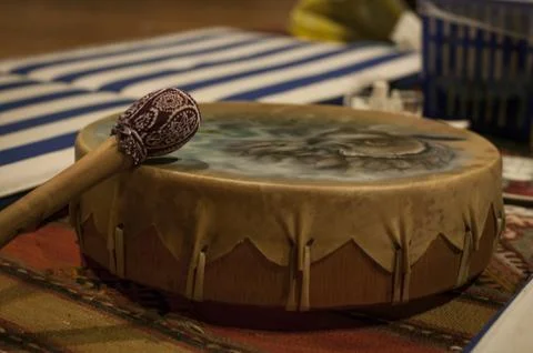 Native american drum with decorated mallet resting on colorful rug Stock Photos