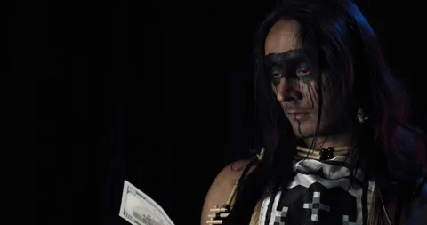 Native american with face paint is holding and dropping a hundred dollar bill 4k Stock Footage 136077597
