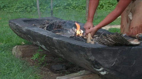 Native American Indian man using primitive tools and fire to dig out log canoe Stock Footage 98767372