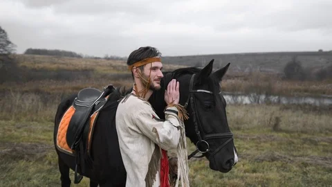 Native American leaned his head against a black horse and stands thoughtfully Stock Footage 124210134