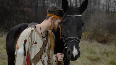 Native American leaned his head against a black horse and stands thoughtfully 動画素材 124211551