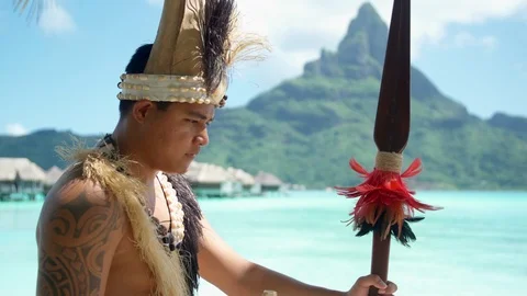 A native islander man blows a conch shell holding a ceremonial spear at a tropic Stock Footage 109750329