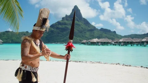 A native islander man blows a conch shell holding a ceremonial spear at a tropic Stock Footage 109750641