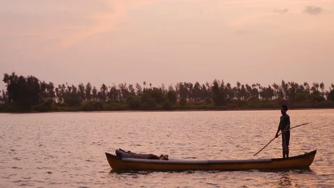 Native person standing on gondola while paddling with stick during sunset, Mulki Stock Footage 145046059