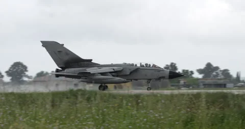 NATO Fighter Bomber Jet Lands on Wet Runway Hidden by Tall Grass with Water Pray Stock Footage 246711258