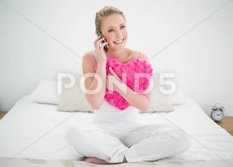Natural content blonde holding heart pillow and phoning Stock Photos