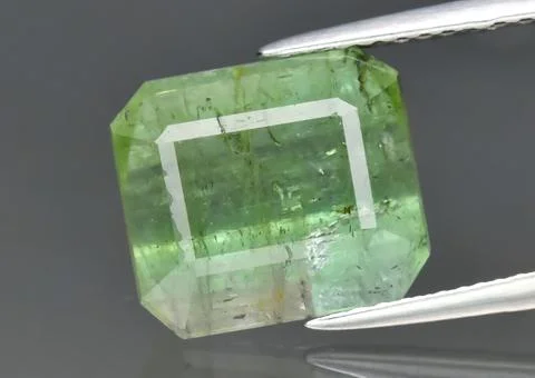 Natural gemstone green Tourmaline in tweezers on a gray background Stock Photos