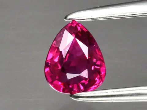 Natural gemstone red ruby in tongs on a gray background 库存照片