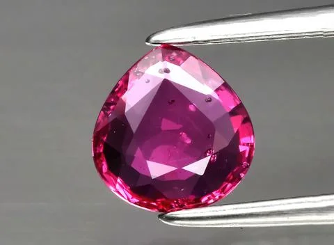 Natural gemstone red ruby in tongs on a gray background Foto stock