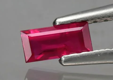 Natural gemstone red ruby in tweezers on a gray background Stock Photos