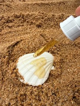 Natural liquid dropping onto a seashell on beach sand concept of nature and b Stock-Fotos