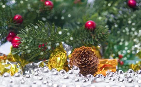 Natural pine cone resting on silver bead garland near gold wrapped candies .. Stock Photos