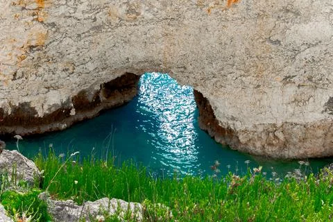 Natural rock archway frames tranquil turquoise water bay with lush green co.. Stock-Fotos
