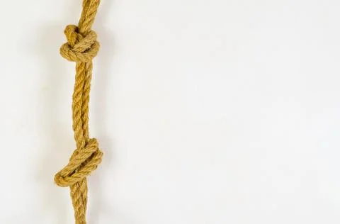A natural rope with knots hangs against the white wall. Yellow rope with smok Stock Photos