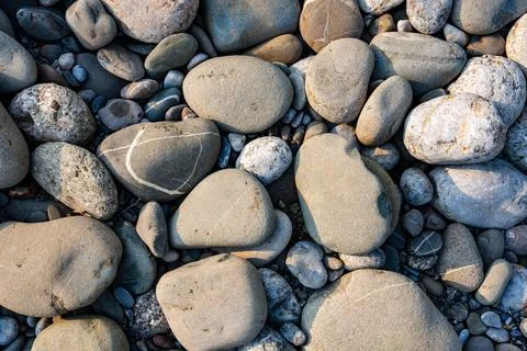 Natural rounded river stones texture with warm daylight detail Stock Photos