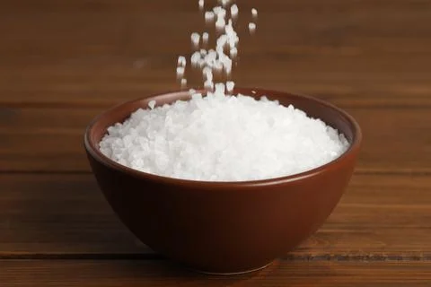 Natural sea salt falling into bowl on wooden table Stock Photos