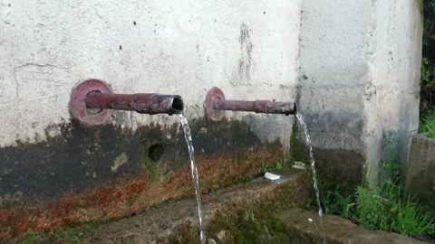 Natural spring water flowing from old metal pipes into stone trough Stock Footage 340123816