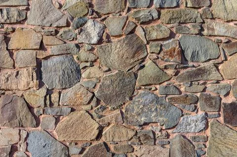 Natural stone wall displays an array of textures and colors under sunlight .. Stock Photos