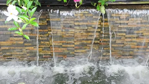 Natural Stone Waterfall Wall Feature with Mist and Flowers. Stockbeeldmateriaal 340047979