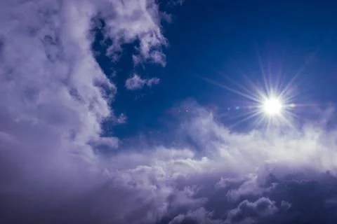 Natural sun shines over clouds in deep blue stormy sky Stock Photos