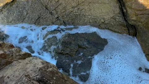 Natural water bubbles form over rocks in the ocean near a rocky shoreline at Stock Footage 339079713