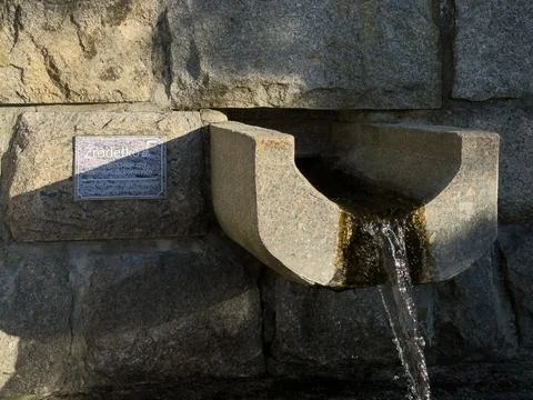 A natural water flow from a rustic stone fountain outdoors displays a peaceful Stock Photos