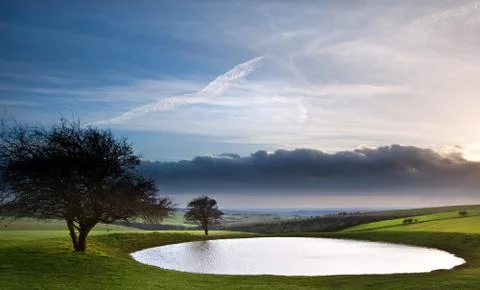Naturally formed dew pond in countryside landscape with moody sky Stock Photos