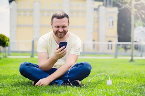 Nature and technology. A man with a beard lies on a green grass with a smartp Foto stock