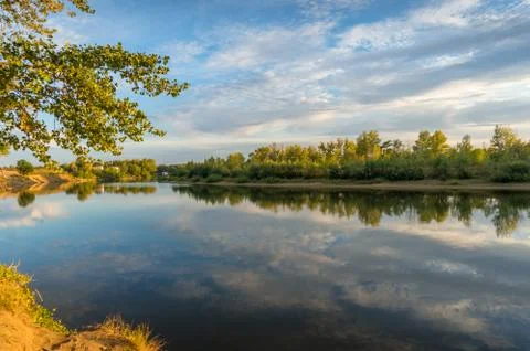 Nature landscape with river and tree lined bank reflected in the water surfac Stock Photos