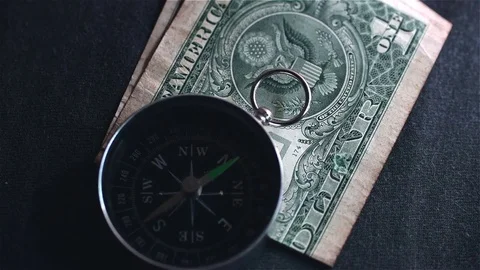 Navigation compass pointing north to a folded dollar bill on a black background Stock Footage 76807787