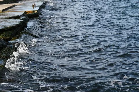 Navy blue sea waves break at stone edge of coastline seaside Stock Photos