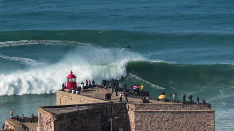 Nazare, Portugal, Surfer Riding Giant Wave Near the Fort of Nazare Lighthouse Stock Footage