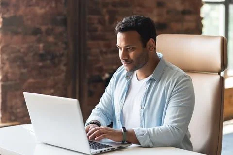 Ndian developer guy is working with a laptop sitting at the desk indoors Foto stock