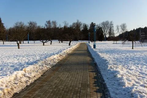 A neat paved path cleared of snow and ice in a snowy city park Stock Photos