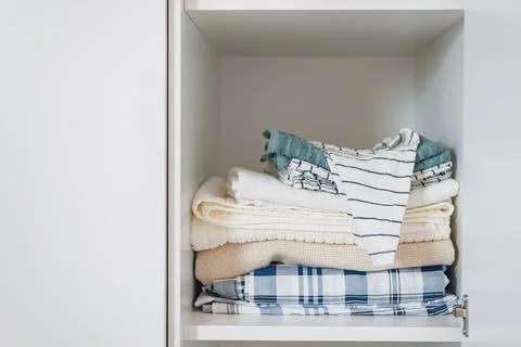 Neat stack of home textiles in light shades lies on a shelf in a white cabinet Stock Photos