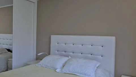 Neatly made double bed with padded white headboard Stock Footage 328851361