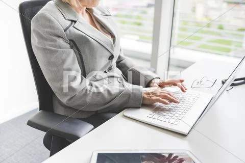 Neck Down View Of Mature Businesswoman Typing At Office Desk