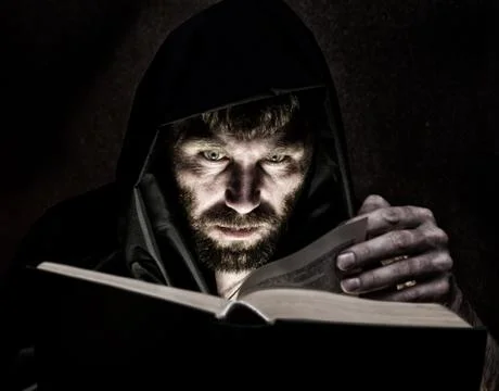 Necromancer casts spells from thick ancient book by candlelight on a dark Stock Photos