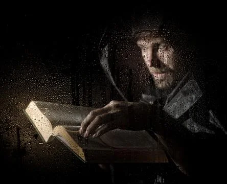 Necromancer casts spells from thick ancient book, behind transparent glass Photos