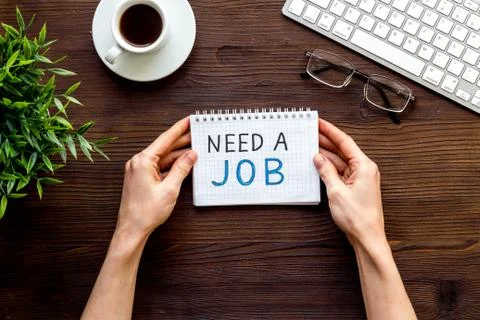 Need a job, looking for. Text in hands on wooden office desk top-down Foto stock