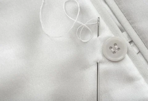 The needle and thread lie on a white cloth. Button on clothes. Seamstress and Stock Photos