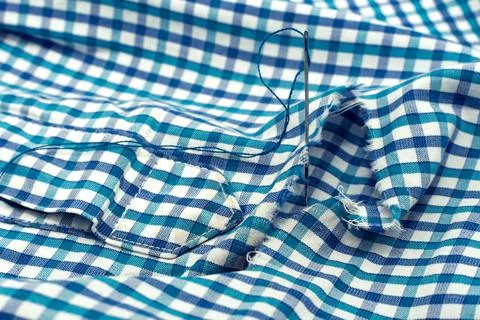 A needle and thread lies on torn or holey clothes. Shirt with a hole. Work .. Stock Photos