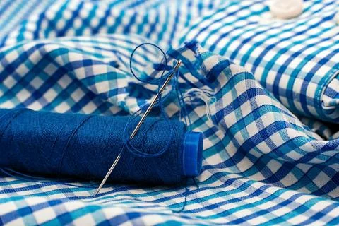 A needle and thread lies on torn or holey clothes. Shirt with a hole. Work .. Stock Photos