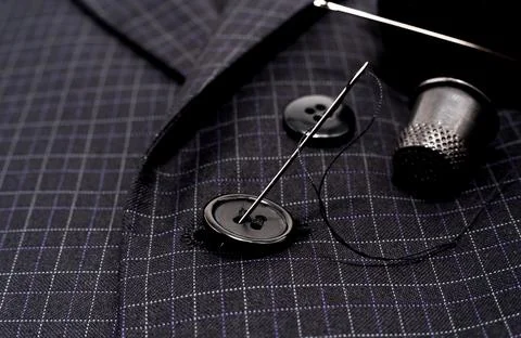 A needle and thread sews up a button on a plaid suit. Thimble. Textile Foto stock