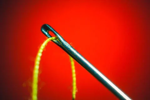 Needle and yellow thread through on orange background Stock Photos