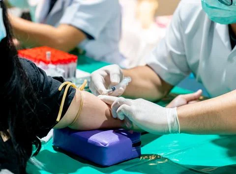 The needle being inserted into the vein while the arm is secured with a yel.. Foto stock