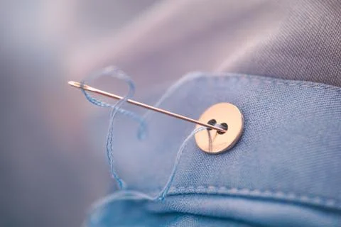 Needle with blue thread sewing button. Stock Photos